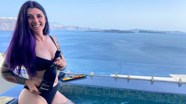 Alexia holds a bottle of champagne in a hot tub overlooking the caldera